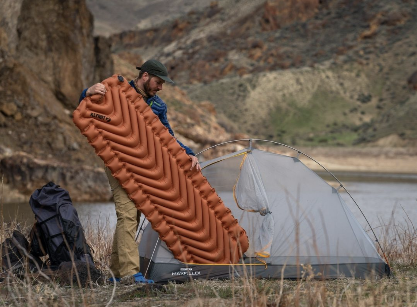 Man holds an orange klymit sleep pad outside a tent