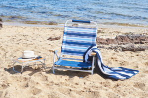 Deluxe beach chair and portable table sit on the beach with a towel and sun hat