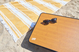 LiFE! portable table on the beach next to a yellow striped towel