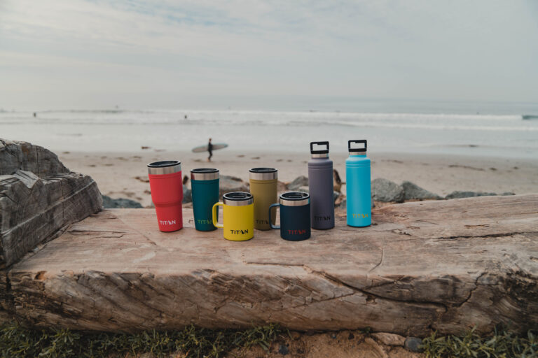 Assortment of Titan cups and drink bottles on a log near the beach